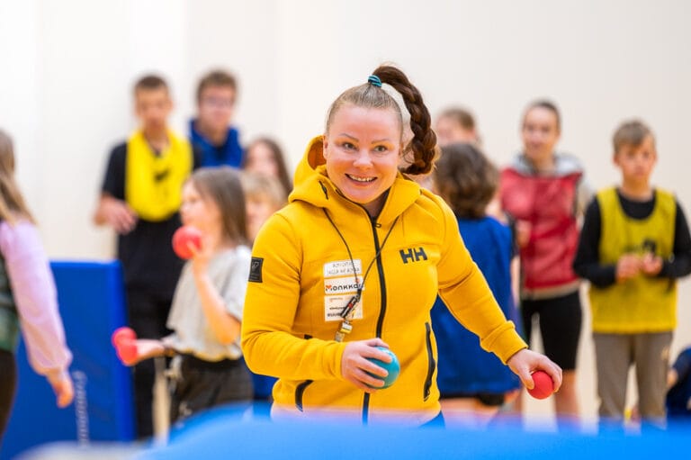 Johanna Kankus-Mikkola liikuntatunnilla. Taustalla koulun lapsia