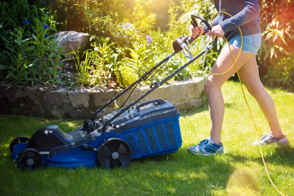 nuori leikkaa nurmikkoa ruohonleikkurilla