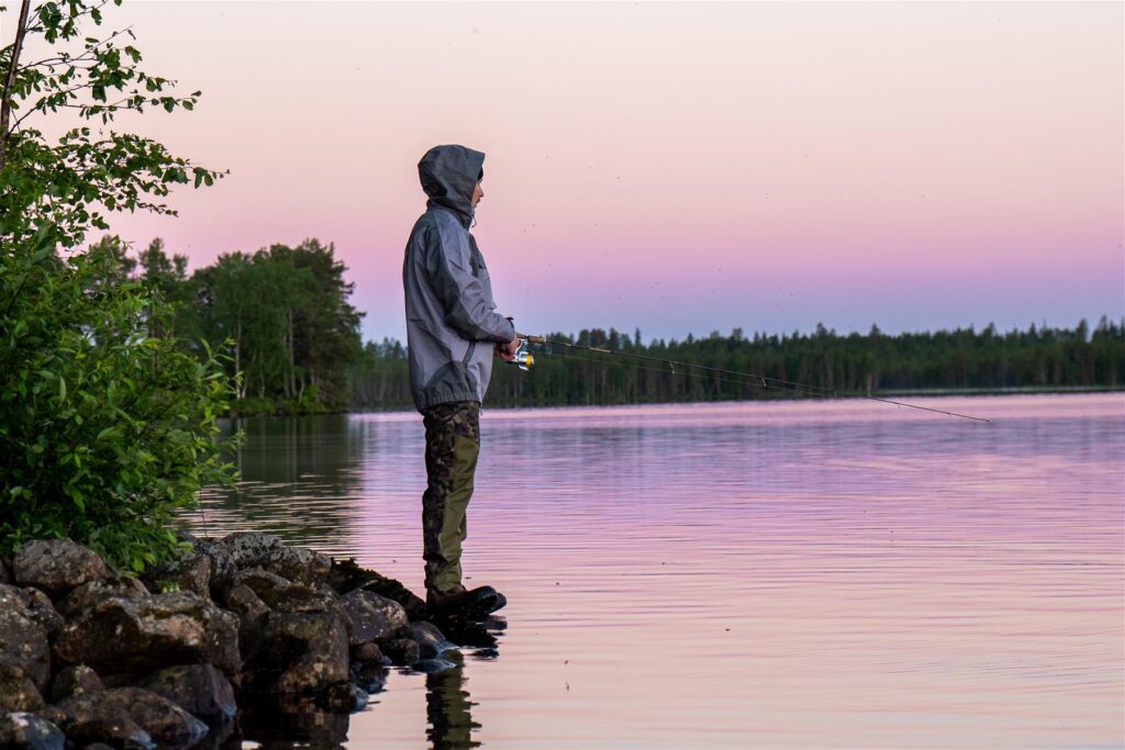 Mies kalastaa kesällä järven rannalla virvelillä.