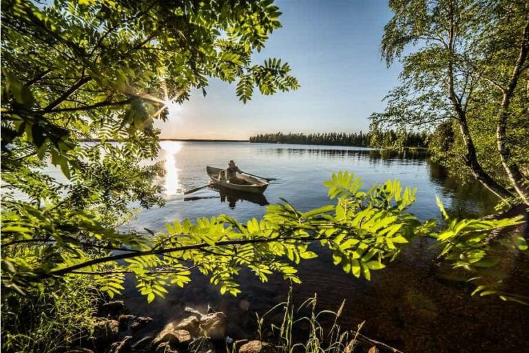 Hattupäinen mies soutaa aurikoisella järvellä.